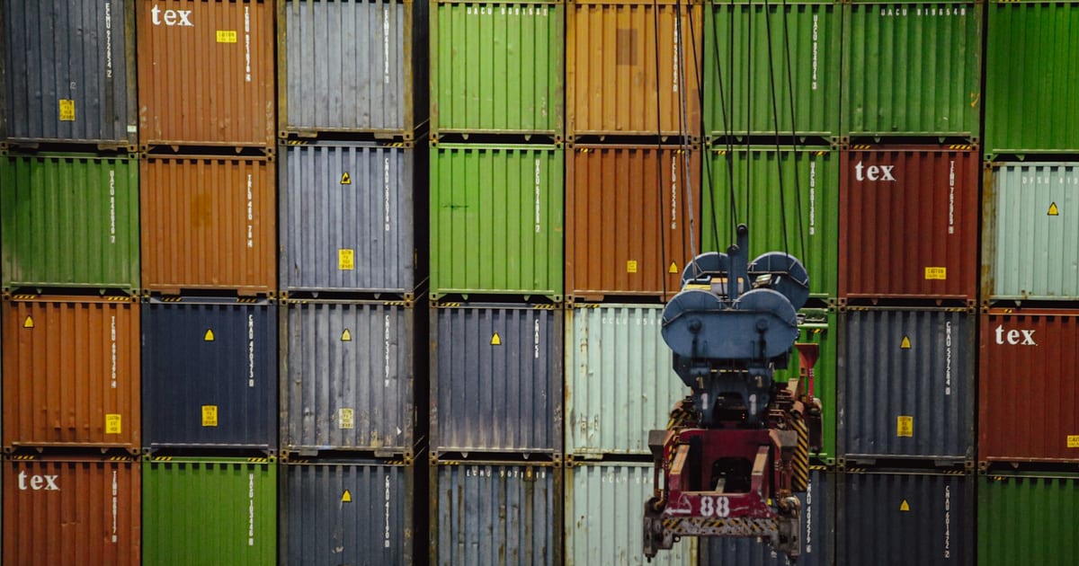 Colorful shipping containers stacked at a port with a crane spreader lifting one, representing international wholesale sourcing
